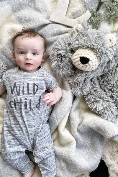 Baby lying on a soft surface with a plush bear lovey made by ClaraLoo. The plush bear features soft gray faux fur and crocheted accents.